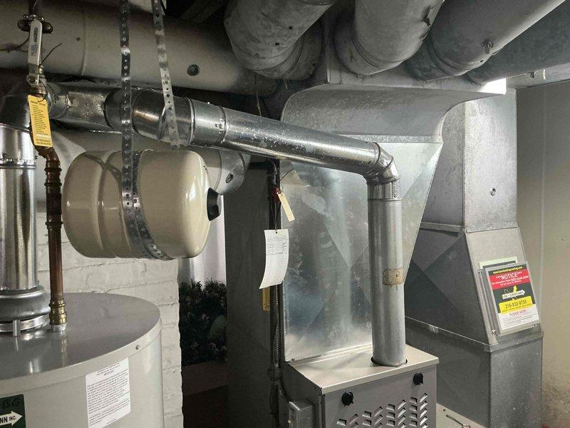 Conducted comprehensive on-site evaluation for add-on air conditioning system installation to existing forced-air heating infrastructure. Assessed current ductwork configuration, plenum connections, and available space in mechanical room to determine optimal placement and integration points for new cooling equipment. Documented existing furnace/air handler setup, including cabinet-style unit with decorative grille, supply and return duct pathways, and insulated ductwork runs to facilitate proper AC coil installation and refrigerant line routing for seamless system integration.