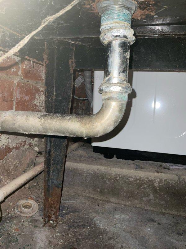 Responded to water leak in basement of century-old residential property. Upon arrival, inspected plumbing system and identified active leak at threaded pipe connection in overhead piping assembly. The galvanized metal elbow joint showed deterioration consistent with the age of the home's infrastructure, with compromised threading allowing water seepage at the connection point.

Shut off water supply to affected area and disassembled the leaking elbow fitting. Cleaned threaded surfaces and removed old deteriorated sealant material. Applied new blue PTFE thread seal tape to male threads according to proper wrapping technique. Reassembled the pipe connection, ensuring proper torque to create watertight seal without over-tightening which could damage aged threading.

Restored water supply and pressure-tested the repair by running water through the system while monitoring the connection point for any signs of moisture or dripping. Confirmed repair was secure with no active leakage detected.