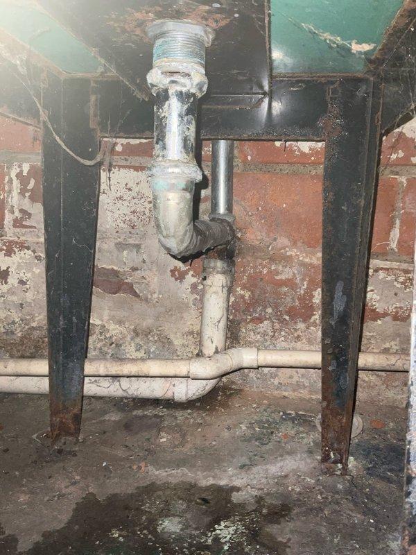 Responded to water leak in basement of century-old residential property. Upon arrival, inspected plumbing system and identified active leak at threaded pipe connection in overhead piping assembly. The galvanized metal elbow joint showed deterioration consistent with the age of the home's infrastructure, with compromised threading allowing water seepage at the connection point.

Shut off water supply to affected area and disassembled the leaking elbow fitting. Cleaned threaded surfaces and removed old deteriorated sealant material. Applied new blue PTFE thread seal tape to male threads according to proper wrapping technique. Reassembled the pipe connection, ensuring proper torque to create watertight seal without over-tightening which could damage aged threading.

Restored water supply and pressure-tested the repair by running water through the system while monitoring the connection point for any signs of moisture or dripping. Confirmed repair was secure with no active leakage detected.
