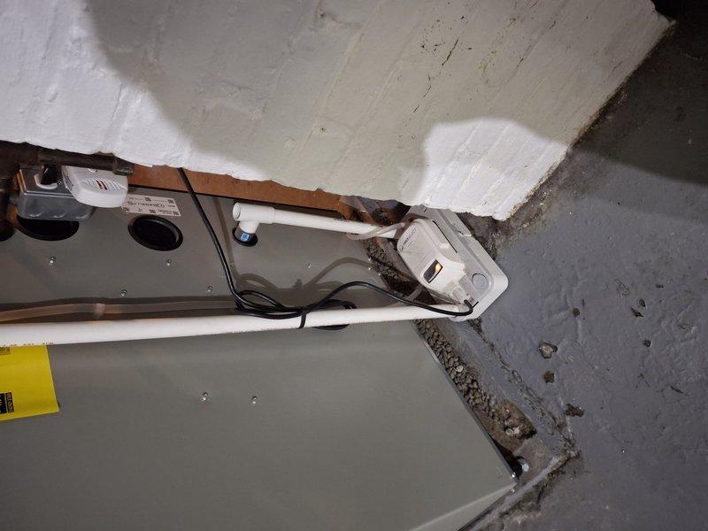 Responded to service call for moisture concerns on 2-3 year old AC unit with reported pipe wicking. Upon inspection, found condensate drainage system experiencing moisture accumulation around indoor air handler unit in basement mechanical room. Concrete floor showed extensive water staining and discoloration patterns indicating ongoing moisture issues. Examined drain pan, condensate lines, and insulation for proper installation and function. Documented conditions with photos showing equipment installation, floor staining, and moisture damage patterns. Recommended monitoring system for proper drainage and potential dehumidification solutions to address basement moisture levels affecting unit performance.