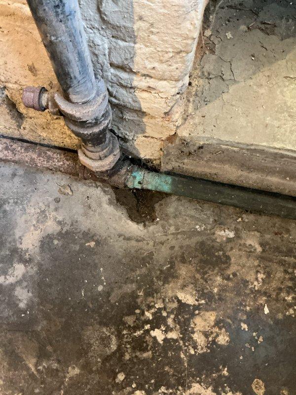 Responded to service call for backed up sink in century-old home. Upon inspection, discovered severely deteriorated plumbing infrastructure in basement area with aged galvanized steel and copper piping showing significant corrosion, verdigris buildup, and rust staining at connection points. The horizontal drain line exhibited extensive deterioration with green-blue corrosion indicative of long-term moisture exposure and material breakdown. Concrete floor surrounding plumbing showed heavy water damage, efflorescence, and staining patterns consistent with chronic drainage issues and possible leaking. Assessed overall condition of aging plumbing system and documented deteriorated pipes, corroded connections, and moisture-damaged basement floor. Due to the advanced age of the plumbing infrastructure and extent of deterioration observed, recommended comprehensive evaluation for potential pipe replacement to address underlying drainage problems and prevent future backups.