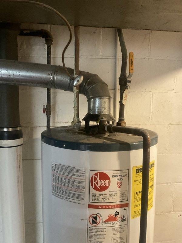 Completed comprehensive plumbing system inspection of residential property, focusing on water heater installation and associated plumbing components. Documented Rheem water heater unit with connected piping systems, including copper supply lines, galvanized steel connections, pressure relief valve assembly, and shut-off valves. Assessed condition of pressure gauge, control valves with blue handles, and brass fittings at pipe junctions. Noted wall deterioration with peeling paint in utility area and photographed all findings for homeowner records.