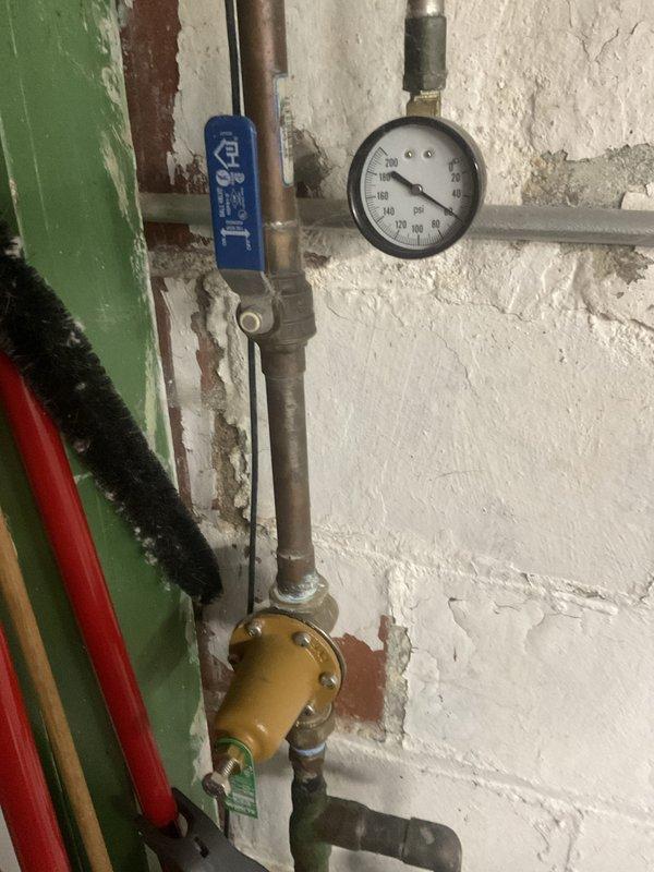 Completed comprehensive plumbing system inspection of residential property, focusing on water heater installation and associated plumbing components. Documented Rheem water heater unit with connected piping systems, including copper supply lines, galvanized steel connections, pressure relief valve assembly, and shut-off valves. Assessed condition of pressure gauge, control valves with blue handles, and brass fittings at pipe junctions. Noted wall deterioration with peeling paint in utility area and photographed all findings for homeowner records.