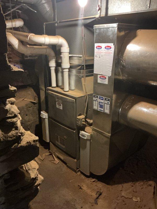 Conducted on-site assessment for air conditioning system addition to existing HVAC infrastructure. Evaluated current gray metal furnace unit with existing white PVC venting configuration and assessed basement mechanical room layout for AC integration compatibility. Documented existing ductwork system, including metallic supply ducts and flexible duct runs, to determine capacity for cooling system tie-in and verified adequate space for condenser unit placement and refrigerant line routing.