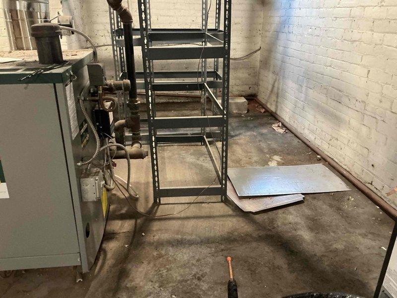 Conducted on-site assessment of boiler system in basement utility room experiencing significant water intrusion and flooding. Documented existing conditions including standing water throughout space, deteriorated wall surfaces with water damage, and compromised structural elements. Evaluated light green boiler unit with associated piping, gauges, and connections to determine impact of flooding on heating system components and provide estimate for necessary repairs or replacement.
