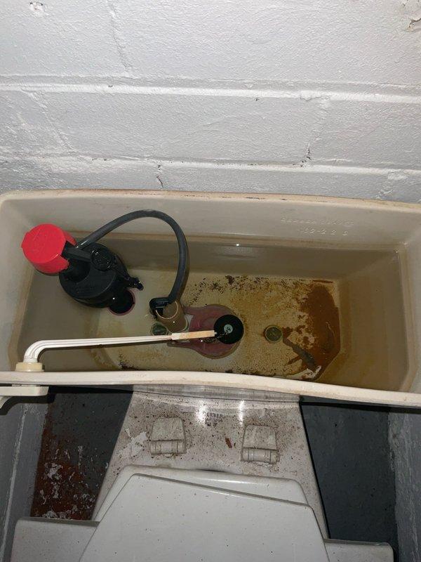 Responded to report of suspected plumbing leak in century-old home with significantly elevated water consumption. Performed diagnostic inspection of second floor and basement toilet systems to identify source of water loss. Upon examination of toilet tank, discovered extensive mineral deposits, rust staining, and corroded internal components consistent with prolonged water seepage. Low water level in tank and deteriorated flapper valve assembly indicated continuous water flow into bowl. Documented condition of flush valve mechanism, float assembly, and tank interior showing advanced corrosion and sediment accumulation affecting proper seal function. Identified failing flapper as primary cause of water waste, resulting in constant running toilet condition that would account for dramatic increase in monthly water usage.