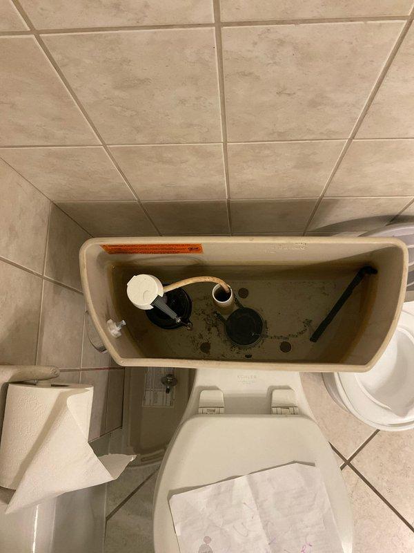 Responded to report of suspected plumbing leak in century-old home with significantly elevated water consumption. Performed diagnostic inspection of second floor and basement toilet systems to identify source of water loss. Upon examination of toilet tank, discovered extensive mineral deposits, rust staining, and corroded internal components consistent with prolonged water seepage. Low water level in tank and deteriorated flapper valve assembly indicated continuous water flow into bowl. Documented condition of flush valve mechanism, float assembly, and tank interior showing advanced corrosion and sediment accumulation affecting proper seal function. Identified failing flapper as primary cause of water waste, resulting in constant running toilet condition that would account for dramatic increase in monthly water usage.