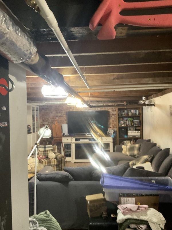 Responded to emergency call for leaking pipe in century-old residential property. Upon arrival, identified active water leak in exposed plumbing system located in basement area near ceiling joists. Documented extensive water damage including brown staining on walls and ceiling surfaces, with visible moisture intrusion through access panel opening. Coordinated with property owner regarding municipal water company shut-off requirements prior to commencing repairs. Assessed aging pipe infrastructure running along upper wall and ceiling sections in finished basement living space. Photographed damage extent and leak source for documentation purposes. Repair work required 5-hour estimated completion time pending water service shut-off coordination.