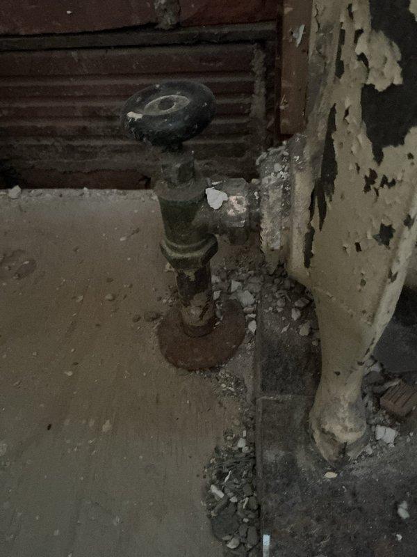 Conducted on-site evaluation for radiator removal and boiler shutdown in residential basement utility area. Assessed existing steam heating system components including aged floor-mounted radiator valve assembly showing significant corrosion and deterioration. Documented current condition of plumbing infrastructure, noting extensive rust on pipe fixtures and mounting plates. Evaluated structural considerations for safe radiator disconnect and removal, including assessment of surrounding floor and wall conditions exhibiting water damage and material deterioration. Photographed existing installation to support estimate preparation for complete radiator removal and proper boiler system shutdown procedures.