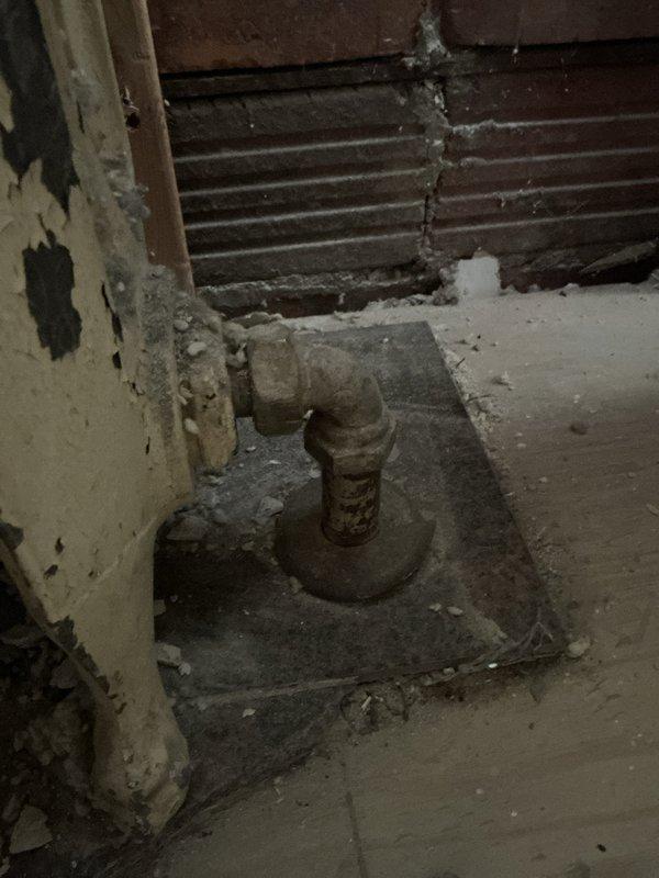 Conducted on-site evaluation for radiator removal and boiler shutdown in residential basement utility area. Assessed existing steam heating system components including aged floor-mounted radiator valve assembly showing significant corrosion and deterioration. Documented current condition of plumbing infrastructure, noting extensive rust on pipe fixtures and mounting plates. Evaluated structural considerations for safe radiator disconnect and removal, including assessment of surrounding floor and wall conditions exhibiting water damage and material deterioration. Photographed existing installation to support estimate preparation for complete radiator removal and proper boiler system shutdown procedures.