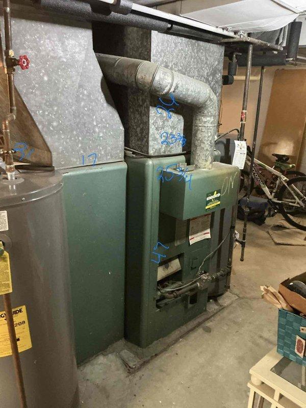 Conducted on-site assessment for replacement estimate of aging 30+ year old furnace system with no cooling capability. Documented existing equipment configuration including green cabinet-style furnace unit, associated ductwork with galvanized sheet metal construction, and adjacent water heating equipment in basement mechanical room. Evaluated current system condition noting visible wear and corrosion on metal components, assessed ductwork connections and routing, and photographed equipment specifications for replacement proposal preparation.