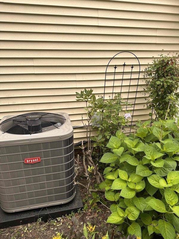 Completed full HVAC system replacement including new furnace, evaporator coil, and outdoor condensing unit. Installed Bryant brand air conditioning condenser with proper positioning on equipment pad against exterior wall, ensuring adequate clearance for airflow and serviceability. Verified system operation with temperature readings confirming proper performance at 159°F on supply ductwork, indicating correct furnace operation and heat exchanger functionality.