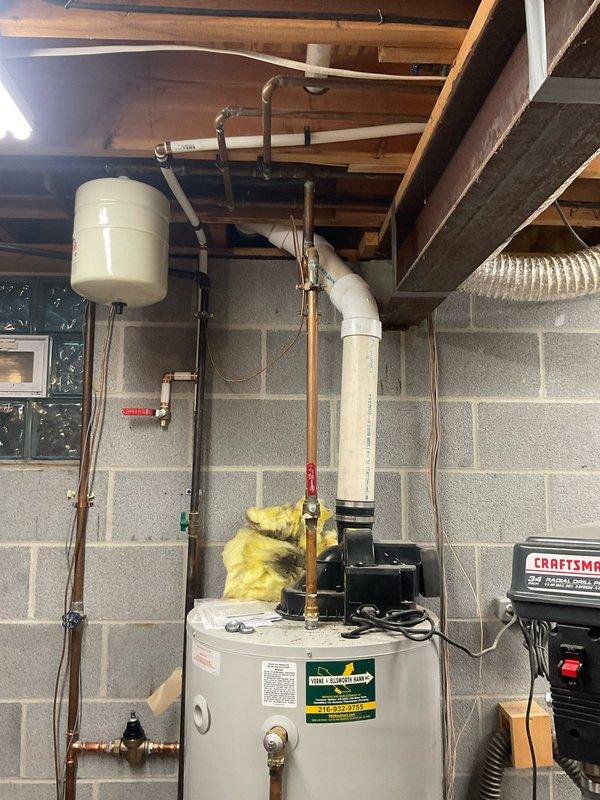 Completed free estimate for water heater replacement in residential basement utility area. Assessed existing white cylindrical tanked water heater installation with connected expansion tank, copper supply lines, PVC venting system, and associated plumbing components. Documented current system configuration including AMTROL expansion tank mounted to ceiling joists, pressure relief valve, and existing piping layout. Provided recommendations for complete water heater replacement at scheduled 8am appointment.