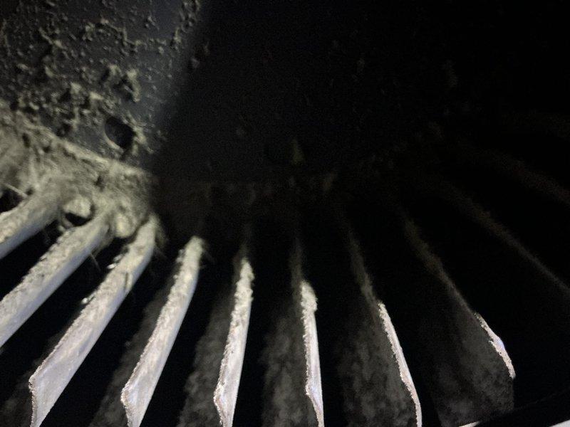 Responded to residential air conditioning service call for 10-year-old system. Upon inspection, discovered evaporator coil completely frozen with heavy ice buildup throughout the fins, indicating restricted airflow or low refrigerant condition. Accessed indoor air handler unit and documented frozen coil assembly and internal components including blower motor and manufacturer specifications. System was not operating properly due to ice accumulation preventing adequate heat exchange. Photographed conditions for documentation purposes showing extent of frost formation on evaporator coils and interior equipment configuration.