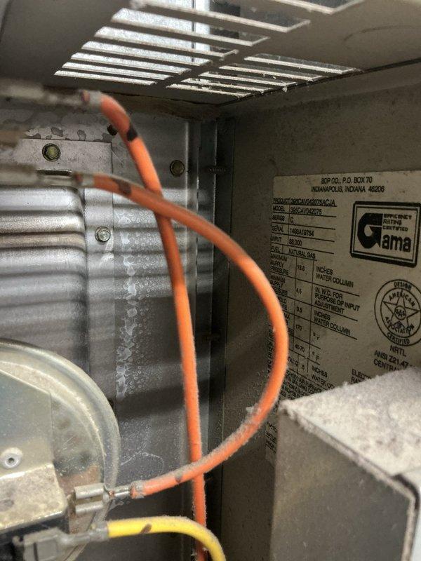 Responded to residential air conditioning service call for 10-year-old system. Upon inspection, discovered evaporator coil completely frozen with heavy ice buildup throughout the fins, indicating restricted airflow or low refrigerant condition. Accessed indoor air handler unit and documented frozen coil assembly and internal components including blower motor and manufacturer specifications. System was not operating properly due to ice accumulation preventing adequate heat exchange. Photographed conditions for documentation purposes showing extent of frost formation on evaporator coils and interior equipment configuration.