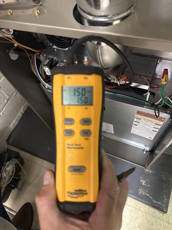 Completed Stage 2 of Bryant furnace installation in basement mechanical room. Performed system diagnostics and commissioning checks using digital multimeter, verifying proper electrical readings at 150 on multiple test points. Confirmed all gas piping connections, flue venting with proper elbow configuration, and clearances around unit meet code requirements. System tested and operational with water heater integration verified.