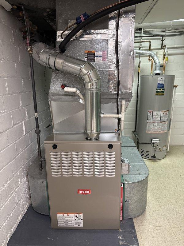 Completed Stage 2 of Bryant furnace installation in basement mechanical room. Performed system diagnostics and commissioning checks using digital multimeter, verifying proper electrical readings at 150 on multiple test points. Confirmed all gas piping connections, flue venting with proper elbow configuration, and clearances around unit meet code requirements. System tested and operational with water heater integration verified.