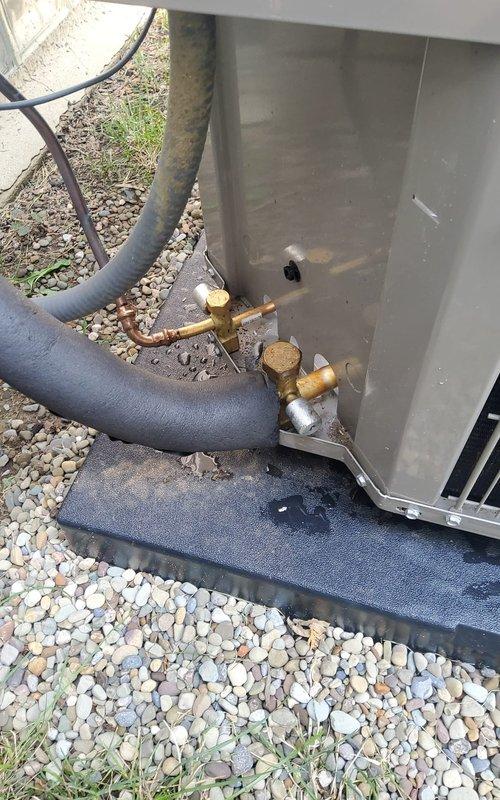 Responded to service call regarding deteriorating insulation on recently installed AC compressor. Upon arrival, performed thorough inspection of outdoor condensing unit and refrigerant line connections. Found black foam insulation on refrigerant lines showing signs of weathering and deterioration at base of unit. Documented condition of brass service valves, copper piping connections, and insulated refrigerant lines with photographs. Inspected unit mounting, gravel pad installation, and overall system installation quality to assess any additional concerns related to the reported deterioration.