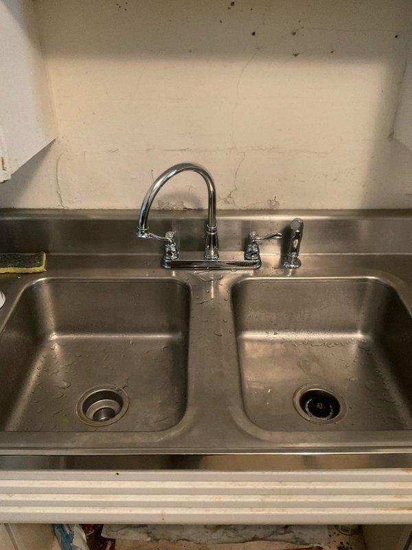 Conducted site assessment for upcoming kitchen faucet replacement on commercial-grade stainless steel double-basin sink. Confirmed existing wall-mounted faucet configuration with two-handle setup and spray attachment requires replacement with customer-supplied fixture compatible with current three-hole mounting arrangement. Documented existing plumbing setup and verified sink compatibility for future installation appointment once new faucet unit is available on-site.
