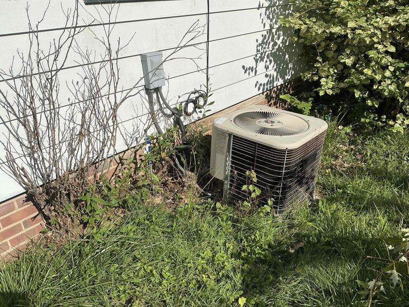 Conducted comprehensive assessment of existing HVAC system for replacement estimate. Evaluated outdoor condensing unit positioned against exterior wall, noting adequate clearance concerns due to overgrown vegetation and landscaping encroachment that may impact airflow and service accessibility. Inspected indoor furnace and air handling equipment located in basement mechanical room, documenting current equipment configuration, ductwork connections, and spatial layout for replacement planning. Photographed both exterior and interior components to provide detailed documentation of existing system conditions and installation parameters for equipment sizing and replacement specifications.