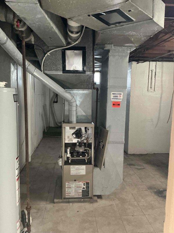 Conducted comprehensive assessment of existing HVAC system for replacement estimate. Evaluated outdoor condensing unit positioned against exterior wall, noting adequate clearance concerns due to overgrown vegetation and landscaping encroachment that may impact airflow and service accessibility. Inspected indoor furnace and air handling equipment located in basement mechanical room, documenting current equipment configuration, ductwork connections, and spatial layout for replacement planning. Photographed both exterior and interior components to provide detailed documentation of existing system conditions and installation parameters for equipment sizing and replacement specifications.