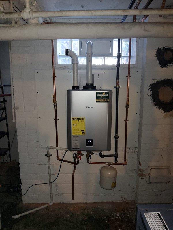 Completed installation of Rinnai tankless water heater system in basement utility area, replacing previous 75-gallon tank water heater. Mounted unit on concrete block wall with proper clearances and structural support. Connected incoming cold water supply and outgoing hot water distribution lines using copper piping with appropriate shutoff valves and fittings. Installed expansion tank below unit to accommodate thermal expansion in closed plumbing system. Configured dual white PVC exhaust and intake venting system extending through exterior wall, ensuring proper combustion air supply and exhaust gas evacuation per manufacturer specifications. Removed existing boiler flue pipe from previous water heater installation. Sealed and capped 75-gallon water heater flue penetration in exterior brick wall to prevent air and moisture infiltration. Verified all gas connections for proper fit and leak-free operation. Tested unit startup sequence, confirmed ignition, and adjusted temperature setting