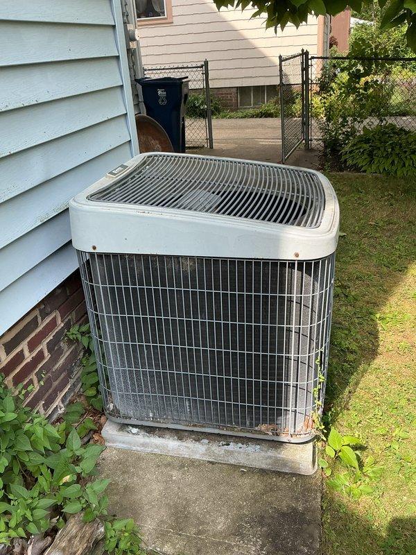 Arrived on-site to assess existing outdoor condensing unit for replacement estimate. Customer requested verbal ballpark pricing prior to formal estimate presentation. Documented current system condition with photos showing aged unit with weathering and discoloration, positioned on concrete pad with cracked surface adjacent to residence exterior.