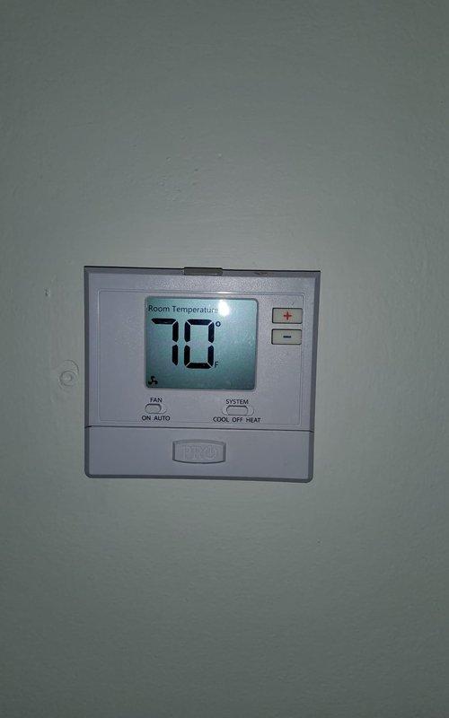 Performed second opinion evaluation on 15-year-old air conditioning system following previous contractor's diagnosis of refrigerant leak. Inspected outdoor condenser unit and found heavy vegetation overgrowth significantly restricting airflow around equipment, which can contribute to reduced efficiency and potential system strain. Verified thermostat operation showing 70°F room temperature setting in cooling mode. Documented excessive plant growth and debris accumulation around condenser requiring clearance for proper operation and serviceability.