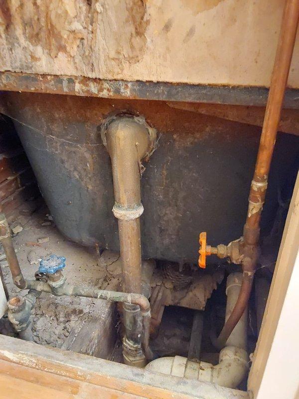 Completed tub waste and overflow replacement requiring two technicians over a two-hour period. Accessed plumbing through wall cavity and subfloor area, removing deteriorated drain assembly affected by extensive water damage. Installed new white PVC drain pipe with proper trap configuration, connecting to existing copper water supply lines and brass fittings. Addressed trap work as needed to ensure proper drainage function. Existing conditions revealed significant water damage to surrounding drywall and wall surfaces with brown discoloration and deterioration, indicating previous moisture intrusion issues. All connections tested and verified leak-free upon completion.