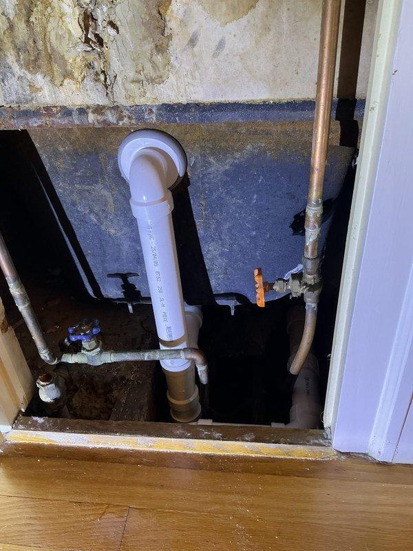 Completed tub waste and overflow replacement requiring two technicians over a two-hour period. Accessed plumbing through wall cavity and subfloor area, removing deteriorated drain assembly affected by extensive water damage. Installed new white PVC drain pipe with proper trap configuration, connecting to existing copper water supply lines and brass fittings. Addressed trap work as needed to ensure proper drainage function. Existing conditions revealed significant water damage to surrounding drywall and wall surfaces with brown discoloration and deterioration, indicating previous moisture intrusion issues. All connections tested and verified leak-free upon completion.