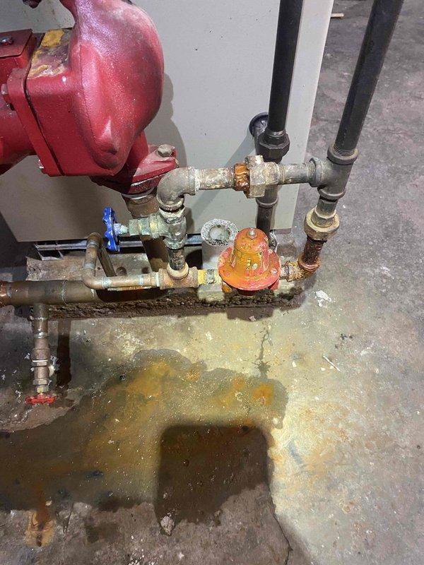 Responded to a boiler leak complaint for complementary diagnostic inspection. Upon arrival, conducted visual assessment of boiler system and associated components. Inspection revealed an EXTROL expansion tank with connected piping assembly showing extensive corrosion and deterioration on galvanized steel pipes and fittings. Documented significant water damage and moisture staining on concrete floor surrounding the base of the piping system, indicating active or recent leakage. Observed rust accumulation on multiple pipe connections, valves, and fittings throughout the assembly. Blue-handled gate valve and orange component connections displayed signs of age-related wear. Photographed corroded piping configuration, compromised fittings, and floor water damage for documentation purposes. Advised customer that this was a diagnostic visit only and does not include repair services, as previously acknowledged.