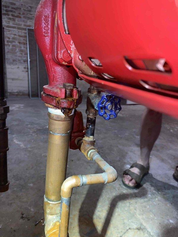 Responded to a boiler leak complaint for complementary diagnostic inspection. Upon arrival, conducted visual assessment of boiler system and associated components. Inspection revealed an EXTROL expansion tank with connected piping assembly showing extensive corrosion and deterioration on galvanized steel pipes and fittings. Documented significant water damage and moisture staining on concrete floor surrounding the base of the piping system, indicating active or recent leakage. Observed rust accumulation on multiple pipe connections, valves, and fittings throughout the assembly. Blue-handled gate valve and orange component connections displayed signs of age-related wear. Photographed corroded piping configuration, compromised fittings, and floor water damage for documentation purposes. Advised customer that this was a diagnostic visit only and does not include repair services, as previously acknowledged.
