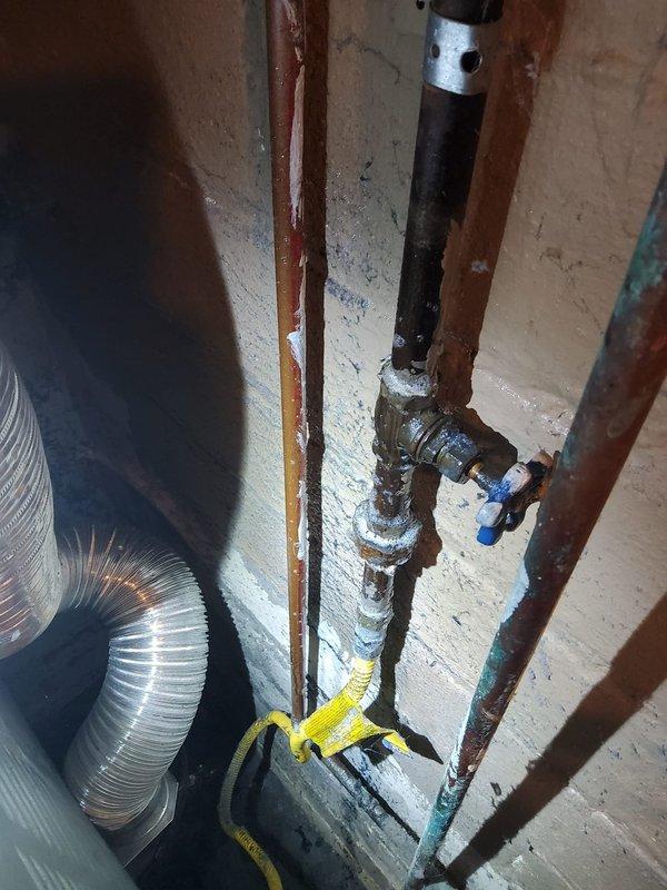 Responded to follow-up service call for remaining gas leak at dryer location after previous repair of two other leaks. Accessed property using lockbox per instructions and performed pressure test to locate source of leak reported by gas company. Inspected gas line connections to dryer, including black iron pipe, shutoff valve with blue handle, and associated fittings in basement utility area. Documented existing conditions and leak location with photographic evidence showing plumbing assembly, flexible ductwork, and floor-level gas connections for repair assessment and landlord approval prior to proceeding with corrective work.