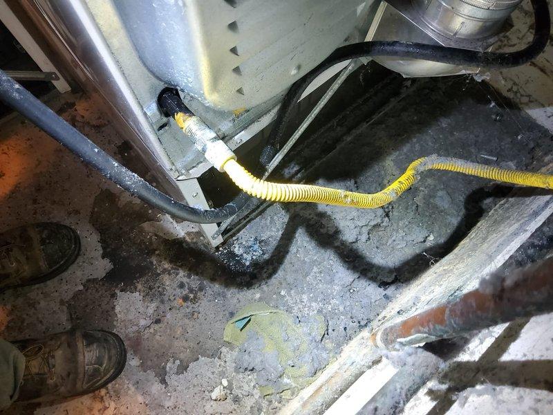 Responded to follow-up service call for remaining gas leak at dryer location after previous repair of two other leaks. Accessed property using lockbox per instructions and performed pressure test to locate source of leak reported by gas company. Inspected gas line connections to dryer, including black iron pipe, shutoff valve with blue handle, and associated fittings in basement utility area. Documented existing conditions and leak location with photographic evidence showing plumbing assembly, flexible ductwork, and floor-level gas connections for repair assessment and landlord approval prior to proceeding with corrective work.