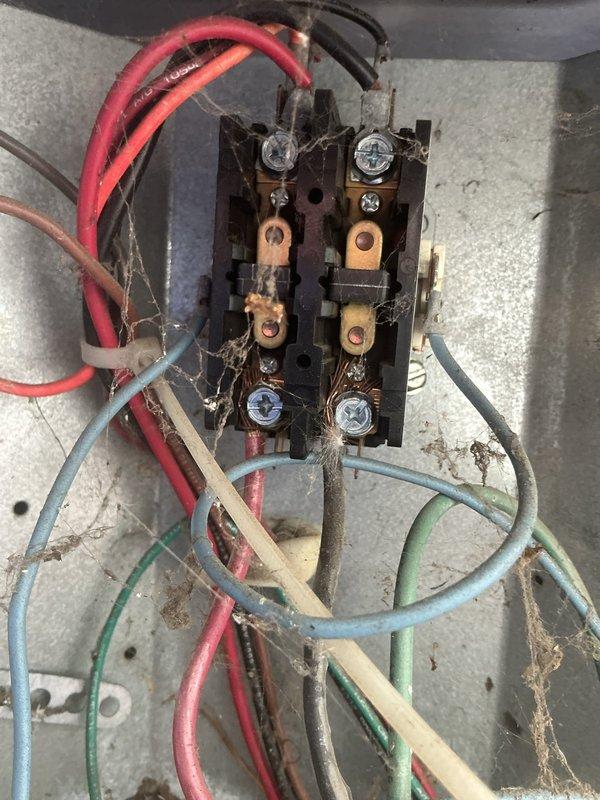 Responded to service call for 20-year-old AC unit running but not cooling. Upon arrival, performed visual inspection of outdoor condensing unit and electrical connections. Found extensive debris accumulation on condenser coil fins and mesh screening, significantly restricting airflow. Heat exchanger fins appeared darkened with heavy buildup of dirt, dust, and organic matter. Leaves and ground debris visible at base of unit. 

Inspected electrical terminal block and wiring connections, noting considerable cobweb accumulation throughout connection panel, indicating lack of recent maintenance. Multiple wire connections showed dust and age-related wear on insulation. All electrical terminations appeared secure despite environmental exposure.

Cleaned condenser coil and removed debris from exterior grille and mesh screening to restore proper airflow. Cleared cobwebs from electrical panel area. Given the unit's age and condition, advised that reduced cooling capacity likely results from comb