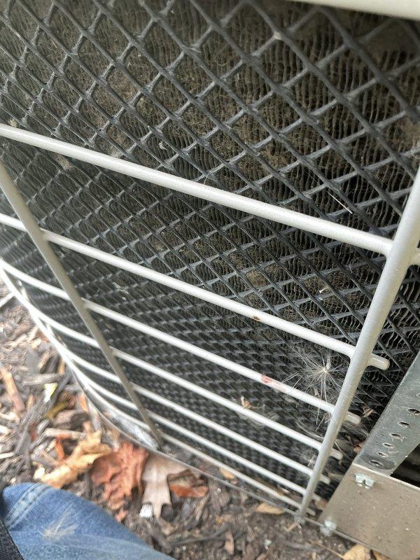 Responded to service call for 20-year-old AC unit running but not cooling. Upon arrival, performed visual inspection of outdoor condensing unit and electrical connections. Found extensive debris accumulation on condenser coil fins and mesh screening, significantly restricting airflow. Heat exchanger fins appeared darkened with heavy buildup of dirt, dust, and organic matter. Leaves and ground debris visible at base of unit. 

Inspected electrical terminal block and wiring connections, noting considerable cobweb accumulation throughout connection panel, indicating lack of recent maintenance. Multiple wire connections showed dust and age-related wear on insulation. All electrical terminations appeared secure despite environmental exposure.

Cleaned condenser coil and removed debris from exterior grille and mesh screening to restore proper airflow. Cleared cobwebs from electrical panel area. Given the unit's age and condition, advised that reduced cooling capacity likely results from comb