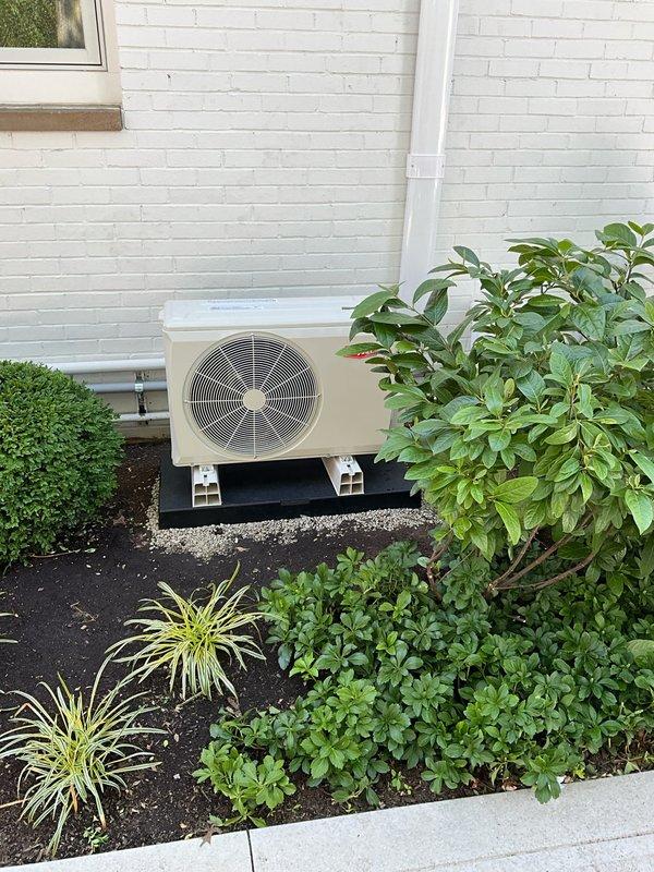 Installed ductless mini-split system to provide heating and cooling for room above garage. Mounted outdoor condenser unit on pad against exterior brick wall with proper clearances and installed indoor air handler unit high on interior wall near ceiling corner. Ran refrigerant line set through wall between units with white line set cover for protection and finished appearance, completed all electrical connections, tested system operation, and verified proper functionality of all components including temperature controls and airflow distribution.