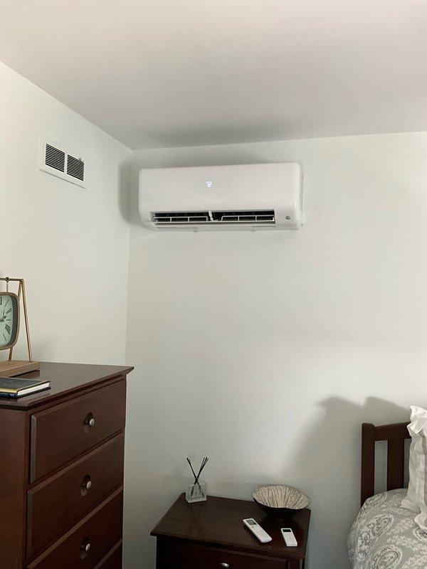 Installed ductless mini-split system to provide heating and cooling for room above garage. Mounted outdoor condenser unit on pad against exterior brick wall with proper clearances and installed indoor air handler unit high on interior wall near ceiling corner. Ran refrigerant line set through wall between units with white line set cover for protection and finished appearance, completed all electrical connections, tested system operation, and verified proper functionality of all components including temperature controls and airflow distribution.