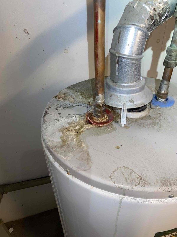 Responded to service call for reported boiler leak at 104-year-old residential property. Upon arrival, conducted thorough inspection of heating system and plumbing infrastructure in basement utility area. Examination revealed the concern was related to the water heater rather than the boiler system. 

Inspected white cylindrical water heater unit and found significant water staining and mineral deposits on top surface of tank, indicating previous moisture issues. Left copper pipe connection showed advanced corrosion and oxidation with reddish-brown discoloration at base fitting, suggesting long-term exposure to moisture. Pressure relief valve assembly on right side examined and found to be intact with proper metallic discharge piping in place.

Traced copper supply lines along wall and ceiling joists to identify potential leak sources. Tagged affected piping section for reference and documentation. Noted varying conditions of copper piping throughout system, with some sections showing 