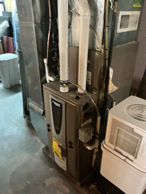 Responded to service call for 10-year-old air conditioning system not cooling and experiencing freeze-up conditions. Upon arrival, performed comprehensive diagnostic evaluation of both indoor and outdoor HVAC components. Inspected York furnace installation in basement mechanical room along with associated ductwork, refrigerant lines, and auxiliary equipment including dehumidifier and wall-mounted air handler. Evaluated outdoor condenser unit, noting overgrown vegetation surrounding equipment which can restrict airflow and reduce system efficiency. Documented current system conditions through photographic evidence showing complete HVAC installation layout and outdoor unit placement. Based on age of equipment, freeze-up symptoms, and overall system assessment, provided detailed estimate for complete HVAC system replacement to address cooling deficiencies and prevent future operational failures.