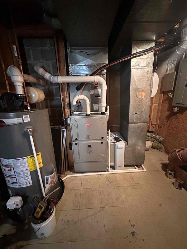 # HVAC Complete System Installation

Successfully completed a full HVAC system replacement in a residential basement utility room. Installed a new Bryant furnace with matching evaporator coil, heat pump system, and Ecobee smart thermostat. The indoor furnace unit was positioned in the basement mechanical room alongside existing water heater, with proper clearances maintained for service access and safety compliance.

Relocated the outdoor heat pump condenser unit to a protected location beneath the deck structure, strategically positioned between two windows for optimal airflow and aesthetic considerations. The unit was mounted on a level pad with gravel base for drainage and stability. Electrical conduit was professionally routed along the exterior wall, and refrigerant lines were properly insulated and connected between indoor and outdoor components.

All ductwork connections were completed with proper sealing, and condensate drainage system was installed with auxiliary pump as neede
