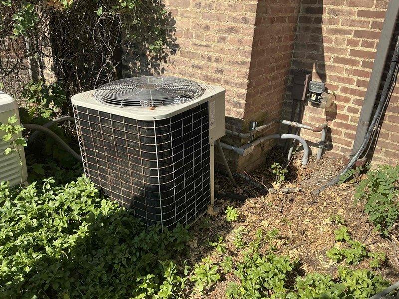 Conducted comprehensive HVAC system evaluation for equipment replacement estimate at residential property. Assessed existing outdoor air conditioning condenser unit positioned against exterior brick wall, documenting unit condition, refrigerant line routing, electrical connections, and clearance requirements. Evaluated interior utility space including attic/basement area with existing ductwork, insulated HVAC components, and utility sink installation to determine replacement system specifications and installation requirements.