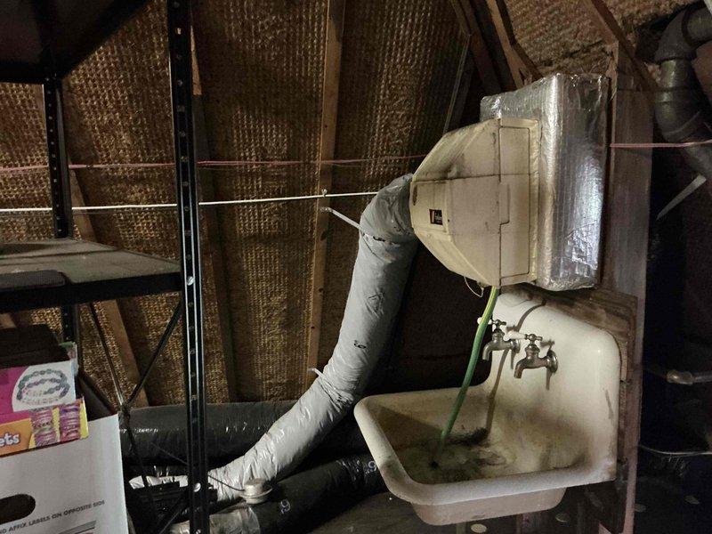 Conducted comprehensive HVAC system evaluation for equipment replacement estimate at residential property. Assessed existing outdoor air conditioning condenser unit positioned against exterior brick wall, documenting unit condition, refrigerant line routing, electrical connections, and clearance requirements. Evaluated interior utility space including attic/basement area with existing ductwork, insulated HVAC components, and utility sink installation to determine replacement system specifications and installation requirements.