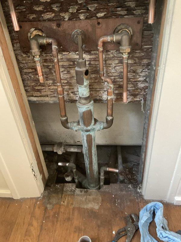 Installed 1/2" press ball valve on existing copper plumbing system accessed through wall cavity. Snaked and cleared drainage obstruction in shower/tub drain line, restoring proper flow. Work involved accessing deteriorated wall cavity with corroded galvanized steel and copper piping, installing new shut-off valve with yellow-handled controls for improved water control, and completing drain cleaning service within one hour of snaking time.