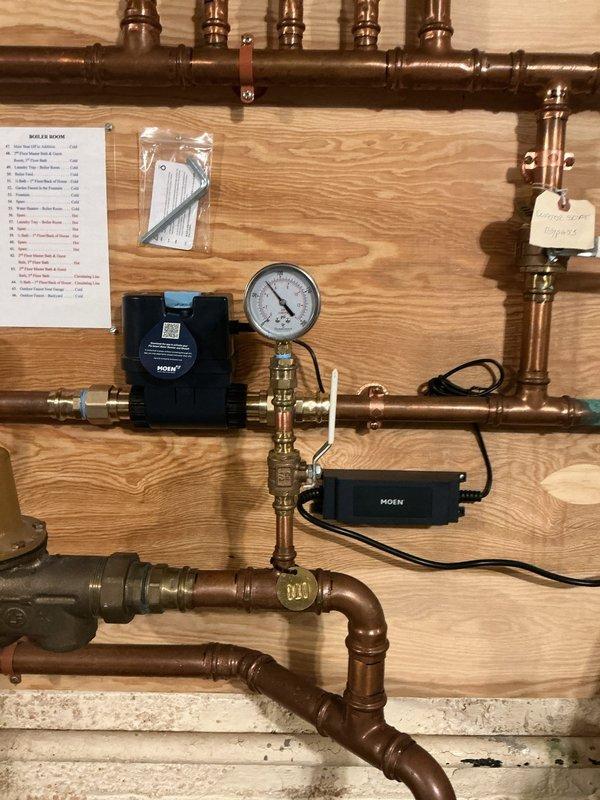 # Moen Flo Smart Water Monitor Installation

Completed installation of Moen Flo whole house smart water monitoring system on residential plumbing distribution panel. Integrated dual electronic monitoring devices into existing copper supply line configuration with brass fittings and pressure regulation components. Installed system pressure gauge for real-time monitoring capability, configured electronic sensors with proper wiring connections, and verified all connections for leak-free operation. Mounted installation documentation and spare components packet on service panel. System tested and operational, providing automated water flow monitoring and leak detection functionality for the entire household plumbing system.