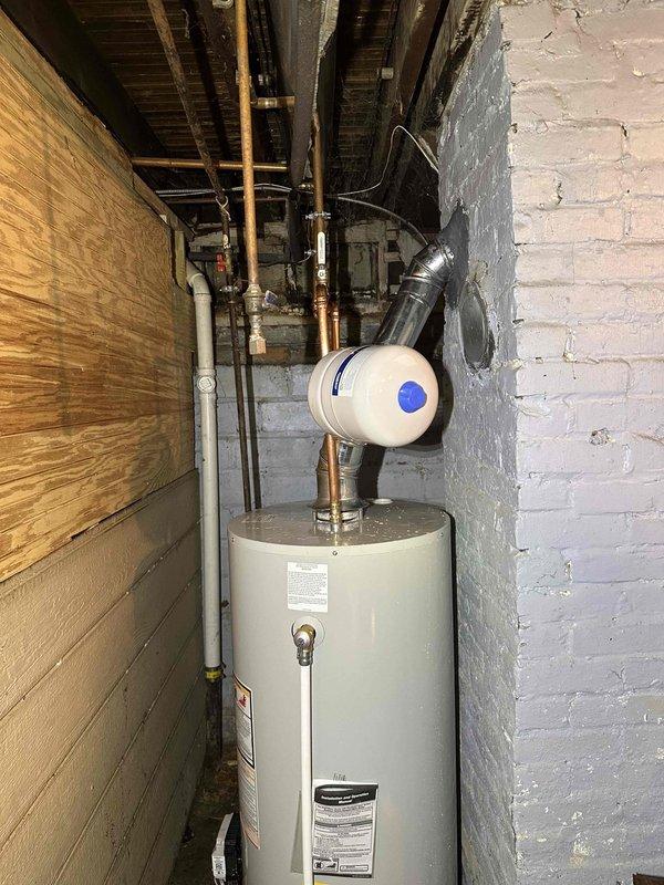 # HVAC Maintenance - Cooling System Service

Performed comprehensive maintenance inspection on residential cooling system located in basement utility area. Upon arrival, accessed mechanical room housing HVAC equipment alongside water heating system in confined space between wooden partition wall and painted brick foundation wall.

Conducted standard maintenance protocol including visual inspection of all accessible components. Examined refrigerant line connections, electrical connections, and condensate drain system. Verified proper clearances around equipment for adequate airflow and safe operation. Inspected ductwork connections including metallic supply plenum with curved transition section extending from air handler unit.

Documented equipment installation environment noting exposed ceiling joists, concrete flooring, and proximity to plumbing infrastructure including copper and PVC water supply lines. Observed humidifier or air quality equipment integrated with HVAC system, connect