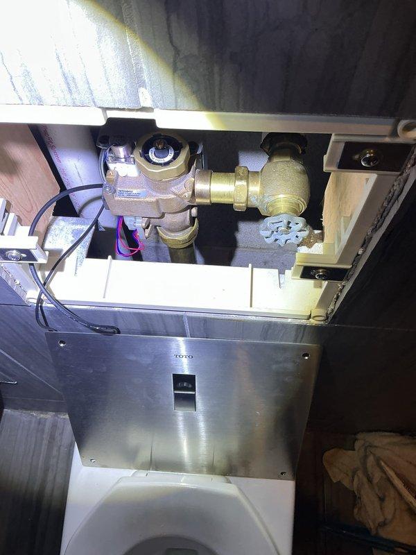 # Warranty Recall - Recurring Toilet Issue

Responded to third service call for recurring toilet malfunction. Upon inspection, discovered significant condensation and frost buildup on the brass flush valve assembly, indicating a temperature differential issue within the TOTO automatic flush system. The excessive moisture accumulation on the central valve body suggests a potential refrigerant line leak or faulty solenoid valve causing abnormal cooling of the brass components. 

Documented the plumbing installation within the wall cavity, noting the valve mechanism, brass fittings, threaded connections, and electronic control panel. The frost pattern on the valve assembly confirms this is the same underlying issue from previous service visits. Photographed the complete assembly including the mounting bracket, compression fittings, and electrical wiring for warranty documentation and further manufacturer review. Recommended escalation to manufacturer for potential recall or replacement of
