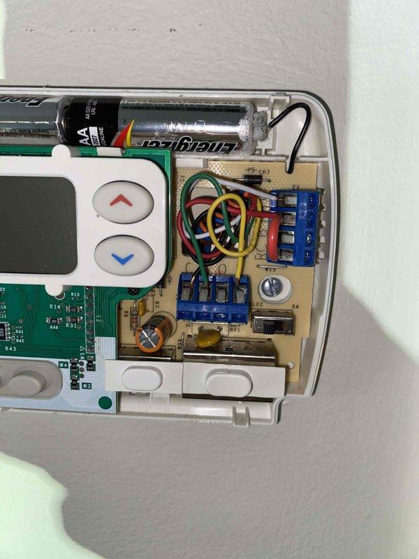 Responded to callback for thermostat malfunction following previous service visit. Inspected White-Rodgers digital thermostat displaying 55°F actual temperature and 68°F setpoint with system in hold mode. Removed thermostat cover and examined internal wiring connections, circuit board components, and AA battery power supply. Verified proper wire terminations at blue terminal blocks, checked for loose connections, and tested thermostat functionality to resolve ongoing temperature control issues.