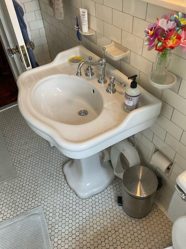 Responded to upstairs bathroom sink leak in century-old home. Upon inspection, identified active leak at supply connection and deteriorated drain piping with heavy corrosion on exposed trap assembly beneath pedestal sink. Repaired leak at supply line connection point and addressed drainage issues related to aged metal piping system. Verified proper water flow and drainage operation upon completion, with all fixtures tested and functioning correctly.