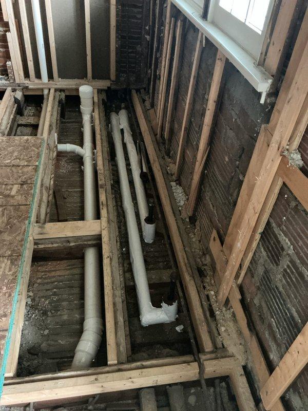 Relocated steam supply and return piping in exposed floor cavity, installed new white PVC drainage lines with proper elbow connections through wooden joist framework. System was filled and pressure tested using boiler gauge monitoring to verify no leaks were present, then all accessible piping was insulated per code requirements.